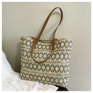 Close-up of woven straw beach bag featuring green geometric patterns and brown leather handles