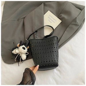 Detail of black laser-cut hollow bucket bag with cute plush bear charm on grey background