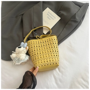 Detail of yellow bucket bag with laser-cut geometric hollows and plush puppy charm