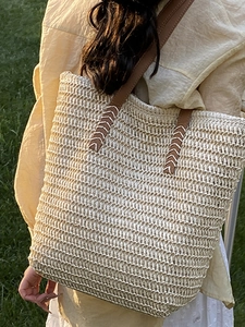 Minimalist straw woven tote bag with brown leather straps shown on a sunny lawn