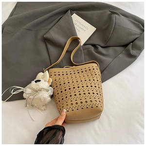Close-up of khaki hollow-out leather bucket bag with cute plush puppy charm detail