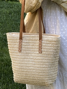 Minimalist woven straw tote bag with brown handles on a model in nature setting
