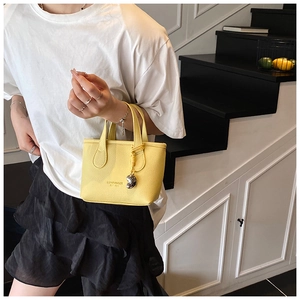 Close-up of yellow pebbled leather handbag with gold logo and heart charm detail