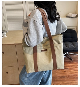 Detail of khaki canvas tote bag with brown handles and leather patch on shoulder