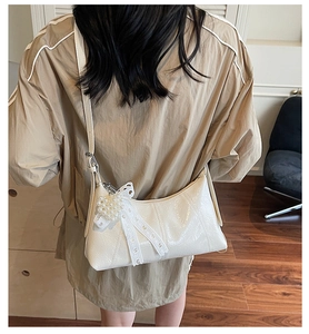 Detail of a creamy white pleated shoulder bag with lace bow and pearl charm accents