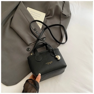 Detail of black lychee grain leather handbag with gold logo and silver heart pendant