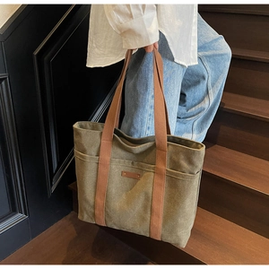Close-up of army green canvas tote bag with brown straps on a wooden staircase
