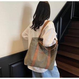 Side view of an olive green canvas tote bag with brown straps worn on the shoulder
