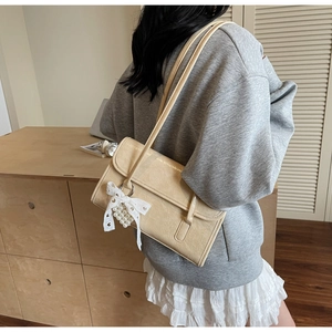 Detail view of beige PU leather shoulder bag featuring a pearl bow pendant and gold lettering