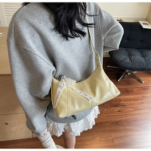Detail of pale yellow glossy underarm bag with pearl heart charm on a model shoulder