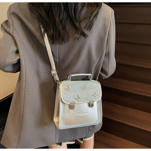 Silver square crossbody bag with butterfly decor and metal buckles worn on a gray suit
