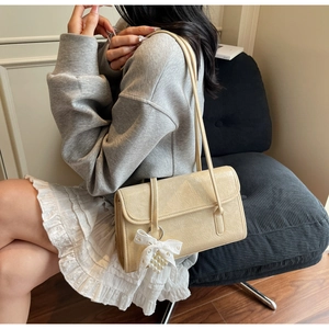 Detail view of beige underarm bag with ruffle texture and lace pearl heart charm
