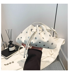 Detail view of white leather bucket bag featuring silver rivets and drawstring closure