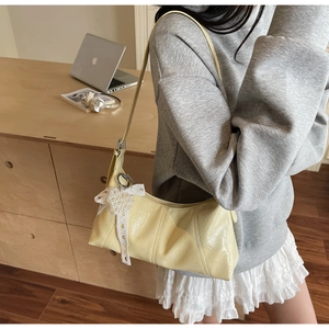 Detail of pale yellow glossy leather underarm bag with pearl bow charm and sleek strap