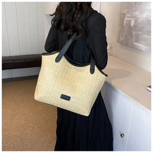 Detail of hand-woven straw tote bag with black leather straps and fashion logo tag