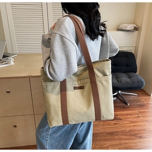 Detail of canvas tote bag showing the side pocket and brown webbing handle reinforcement