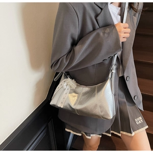 Detailed view of silver metallic shoulder bag with pearl bow decoration on stylish outfit