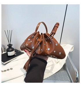 Detail of caramel drawstring bucket bag with silver studs and polished PU leather surface