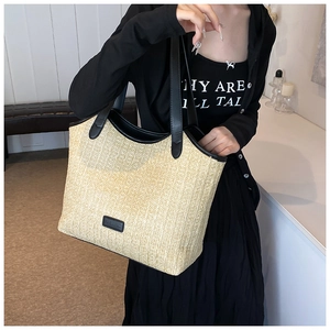 Detailed close-up of woven straw tote bag with black leather straps and fashion label