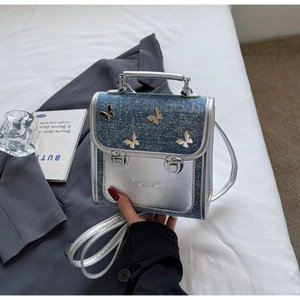 Detail of square denim and silver leather bag with metal butterfly accents and buckles
