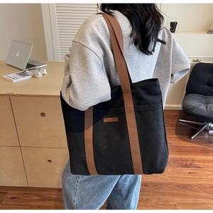 Large black canvas tote bag with brown straps shown in a minimalist office setting