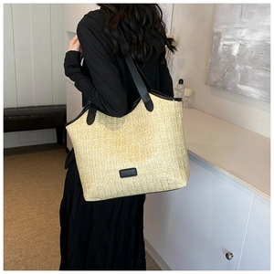 Detailed view of beige straw tote bag with black leather straps on a fashion model