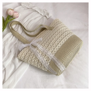 Detail of beige straw tote bag featuring intricate white lace overlay and bow decoration