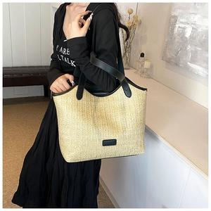 Detail of hand-woven straw tote bag with black leather straps and fashion label