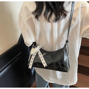 Detail of black glossy shoulder bag featuring white lace bow and pearl heart charm decor