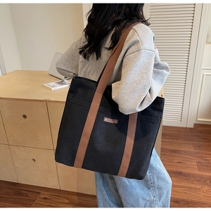 Detail of black canvas tote bag with brown straps and leather patch on model