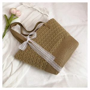 Close-up of khaki woven beach tote bag with a white lace ribbon bow on a white cloth