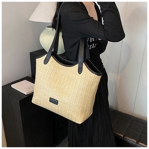 Close-up of straw woven tote bag with black leather handles and fashion logo patch