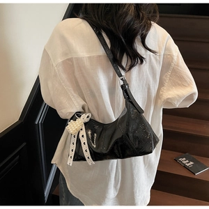 Detail view of black glossy patent leather shoulder bag with lace bow and pearl charm