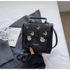 Detail view of black leather handbag with silver butterfly accents and rhinestone decor