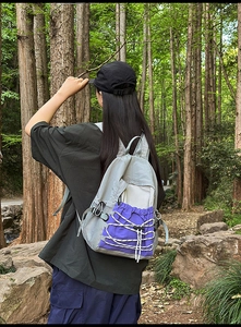 Outdoor waterproof backpack with grey and purple color-blocking shown in a forest setting