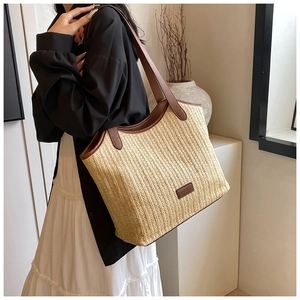 Detail of large straw woven tote bag with brown leather handles and fashion logo patch