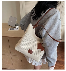 Detail of knit tote bag with brown leather trim, decorative label and cute bear charm
