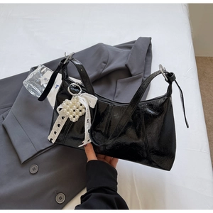 Detail of black glossy shoulder bag with lace pearl heart charm on grey fabric