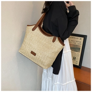 Detail of a large straw tote bag with brown leather straps worn on a shoulder
