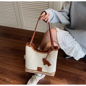 Detail of knit tote bag with brown leather handles and a horse-shaped charm