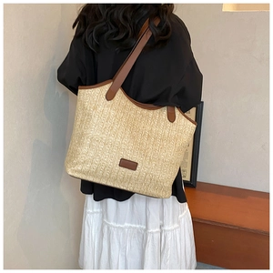 Detail of hand-woven beige straw tote bag with brown leather handles and brand tag