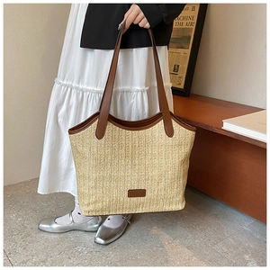 Detail of hand-woven straw tote bag showing brown leather handles and textured weave