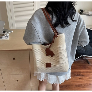 Detail of knit tote bag with brown leather shoulder straps and dog-shaped charm