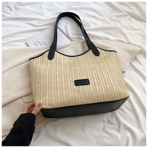 Détail du grand sac cabas en paille tissée avec poignées en cuir noir et logo sur lit blanc