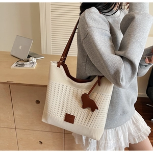 Close-up of beige knitted tote bag with brown leather trim and cute puppy charm