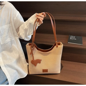 Detail of crochet knit tote bag with brown leather strap and animal charm on wooden steps