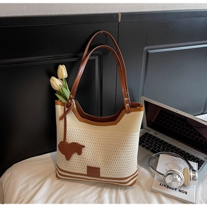 Detail of cream knit tote bag with brown stripes and horse charm on a cozy bed