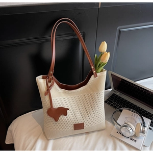 Close-up of cream knit tote bag featuring brown leather handles and a horse charm