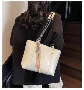 Detail of a beige leather tote bag with silver chain strap and pink tassel on a model