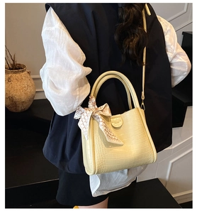 Détail du sac seau beige à motif crocodile avec foulard décoratif et bandoulière